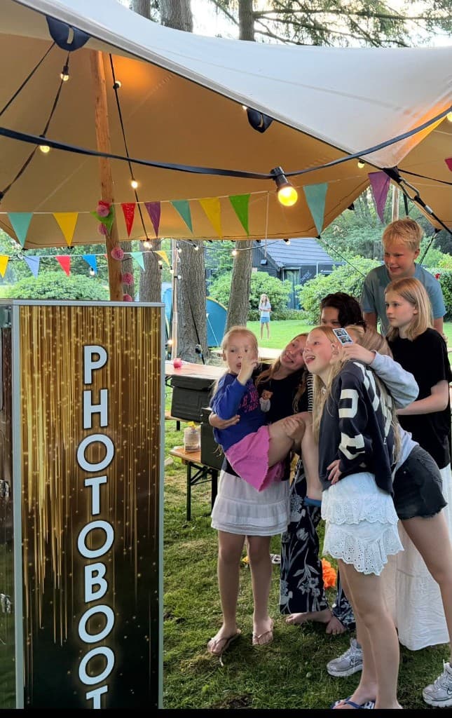 Kinderen poseren bij de Photobooth Kiosk onder een feesttent met feestverlichting