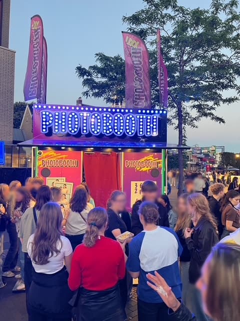Publiek bij de roze PHOTOBOOTH XXL in de avond met beachvlaggen